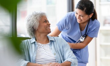 A female patient in a wheelchair smiling at a female nurse